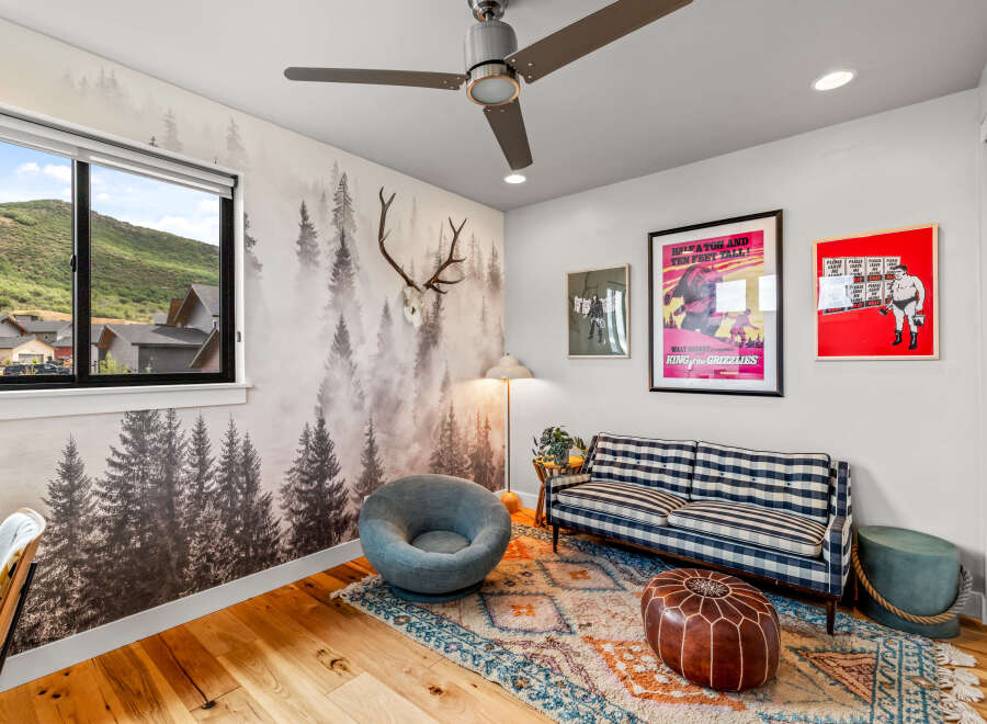 Experience a unique living space with a captivating forest-themed wallpaper and a stunning mountain view from the large window.