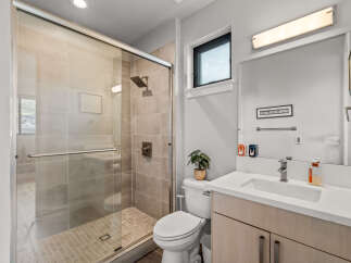 Experience modern comfort in this beautifully appointed bathroom, featuring a sleek glass-enclosed shower with tiled walls and a convenient handheld showerhead.