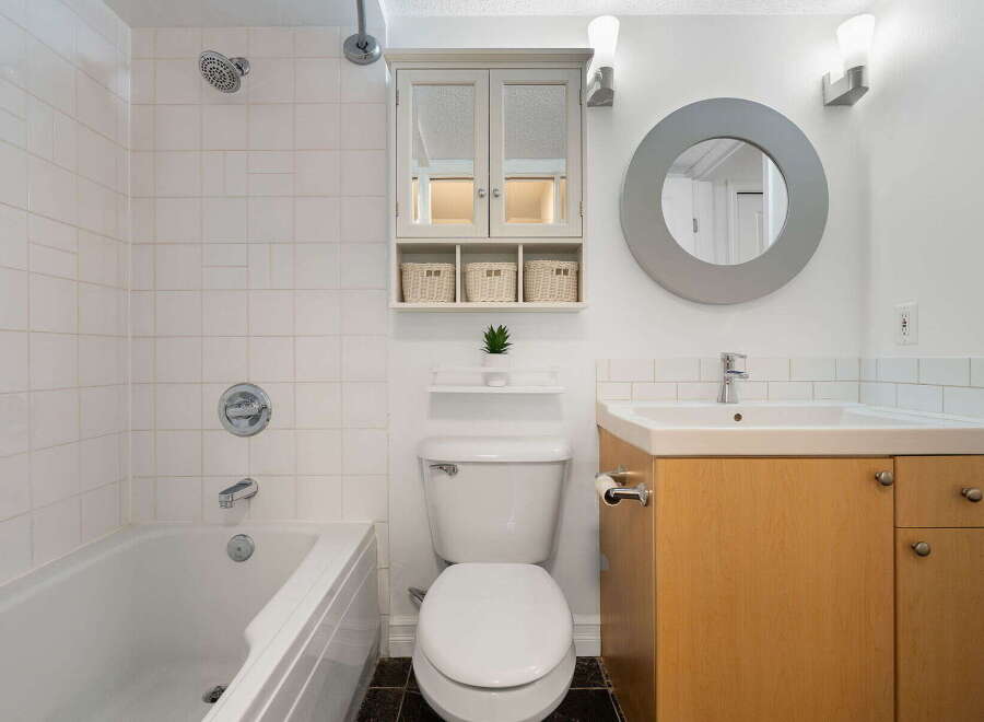 This bright and clean bathroom features a spacious bathtub with white tiled walls, a modern toilet, and a vanity with a sink and ample storage.
