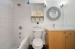 This bright and clean bathroom features a spacious bathtub with white tiled walls, a modern toilet, and a vanity with a sink and ample storage.