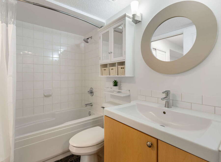 This bright and clean bathroom features a spacious bathtub with a tiled shower surround, perfect for relaxing.