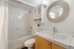This bright and clean bathroom features a spacious bathtub with a tiled shower surround, perfect for relaxing.
