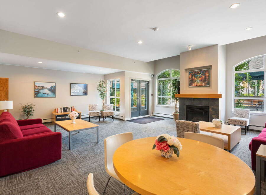 This inviting common area features a cozy fireplace, comfortable seating arrangements, and large windows that flood the space with natural light.