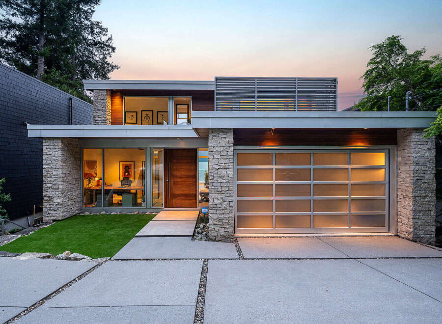 Experience modern luxury in this stunning home featuring a sleek design with stone accents and a frosted glass garage door.