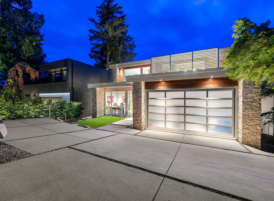 Experience modern luxury in this stunning residence featuring a sleek glass garage door and natural stone accents.