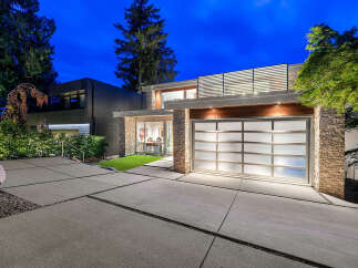Experience modern luxury in this stunning residence featuring a sleek glass garage door and natural stone accents.