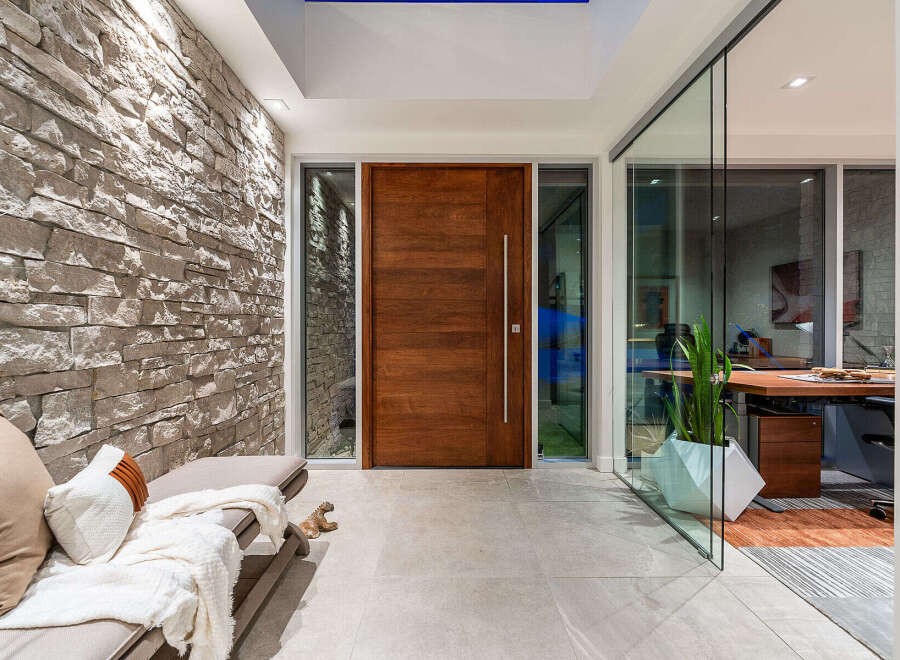 Experience modern luxury with this stunning entryway featuring a striking stone accent wall and a sleek, oversized wooden door.