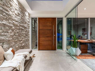 Experience modern luxury with this stunning entryway featuring a striking stone accent wall and a sleek, oversized wooden door.