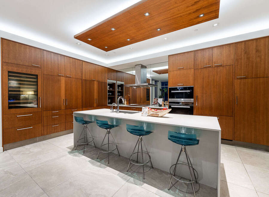 Experience luxury in this modern kitchen featuring sleek, warm wood cabinetry that extends to the ceiling, creating a seamless and sophisticated look.