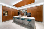 Experience luxury in this modern kitchen featuring sleek, warm wood cabinetry that extends to the ceiling, creating a seamless and sophisticated look.