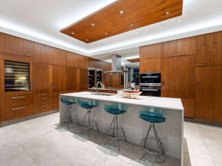 Experience luxury in this modern kitchen featuring sleek, warm wood cabinetry that extends to the ceiling, creating a seamless and sophisticated look.