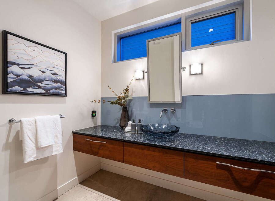 This modern bathroom features a floating vanity with rich wood cabinetry and a sleek granite countertop.
