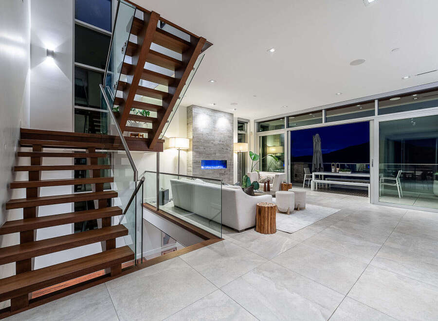 Experience modern luxury in this stunning living space featuring a floating wooden staircase with glass railings.