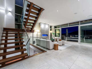 Experience modern luxury in this stunning living space featuring a floating wooden staircase with glass railings.