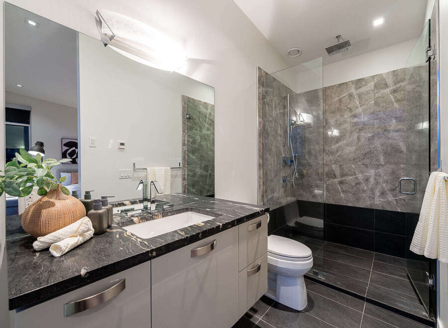 Experience modern luxury in this stunning bathroom featuring a sleek vanity with a granite countertop and a spacious glass-enclosed shower with marble tile accents.