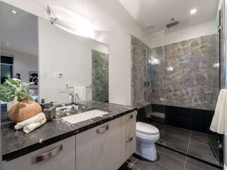 Experience modern luxury in this stunning bathroom featuring a sleek vanity with a granite countertop and a spacious glass-enclosed shower with marble tile accents.