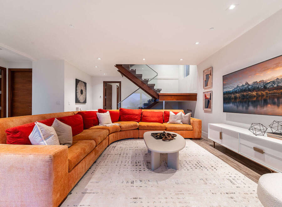 Experience modern luxury in this stunning living room, featuring a large, curved sectional sofa in a warm orange hue complemented by plush red and patterned throw pillows.