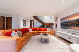 Experience modern luxury in this stunning living room, featuring a large, curved sectional sofa in a warm orange hue complemented by plush red and patterned throw pillows.