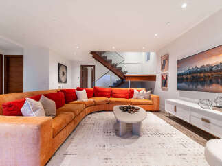 Experience modern luxury in this stunning living room, featuring a large, curved sectional sofa in a warm orange hue complemented by plush red and patterned throw pillows.