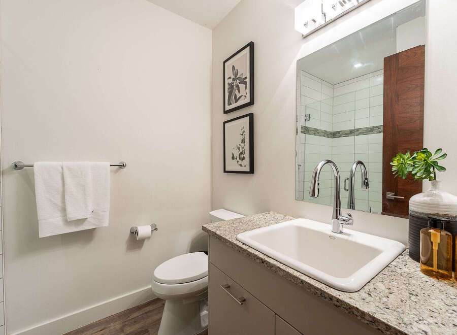 This modern bathroom features a sleek vanity with a granite countertop, complemented by a clean white sink and a contemporary faucet.