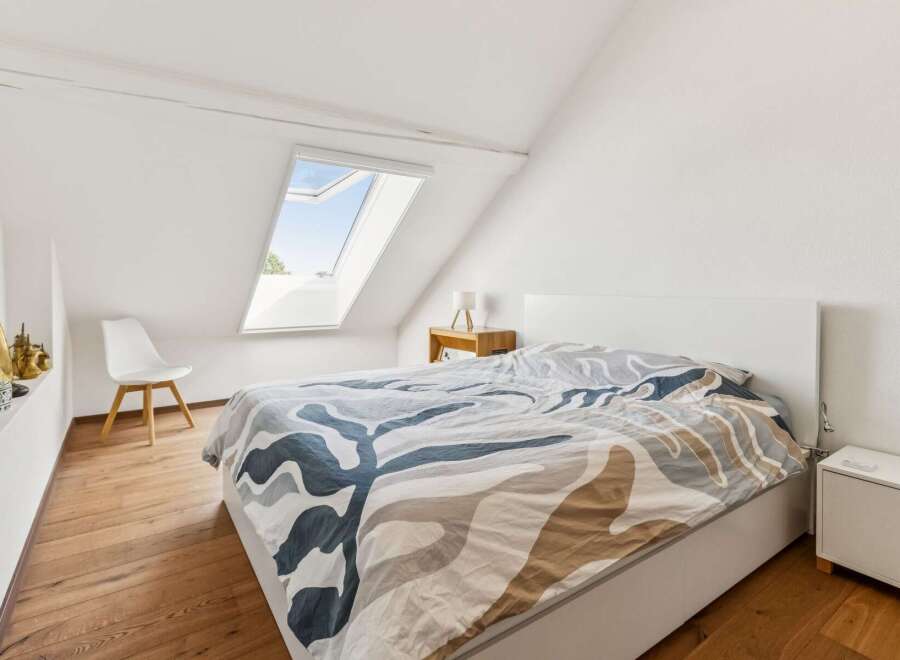 Discover this charming attic bedroom featuring a comfortable bed with a unique patterned duvet.