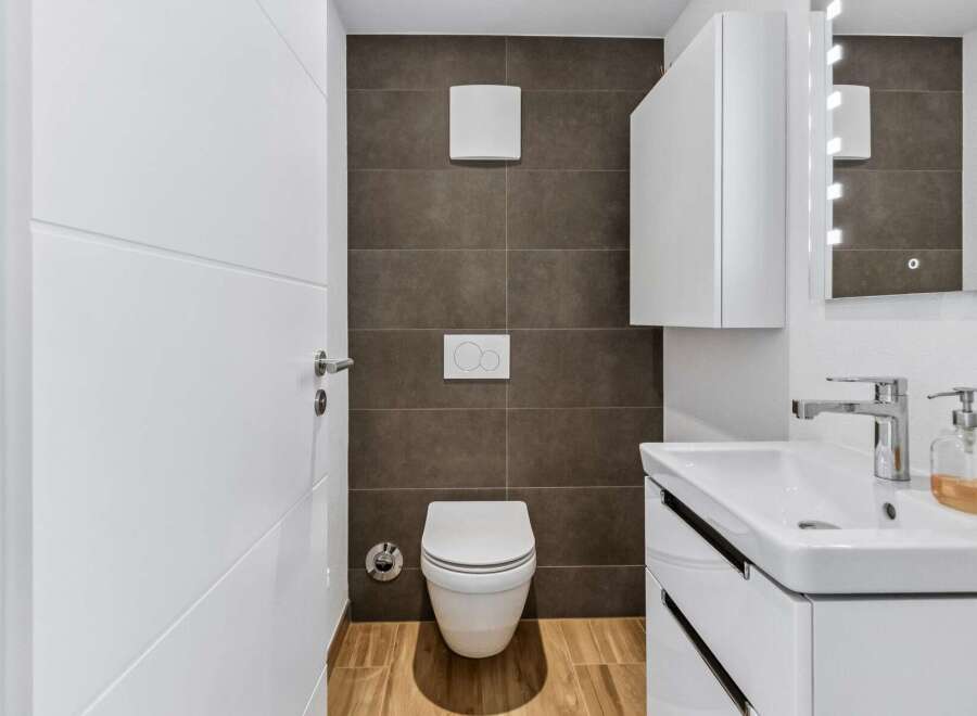 This modern bathroom features a sleek white toilet with a concealed cistern and a stylish white vanity with a vessel sink.