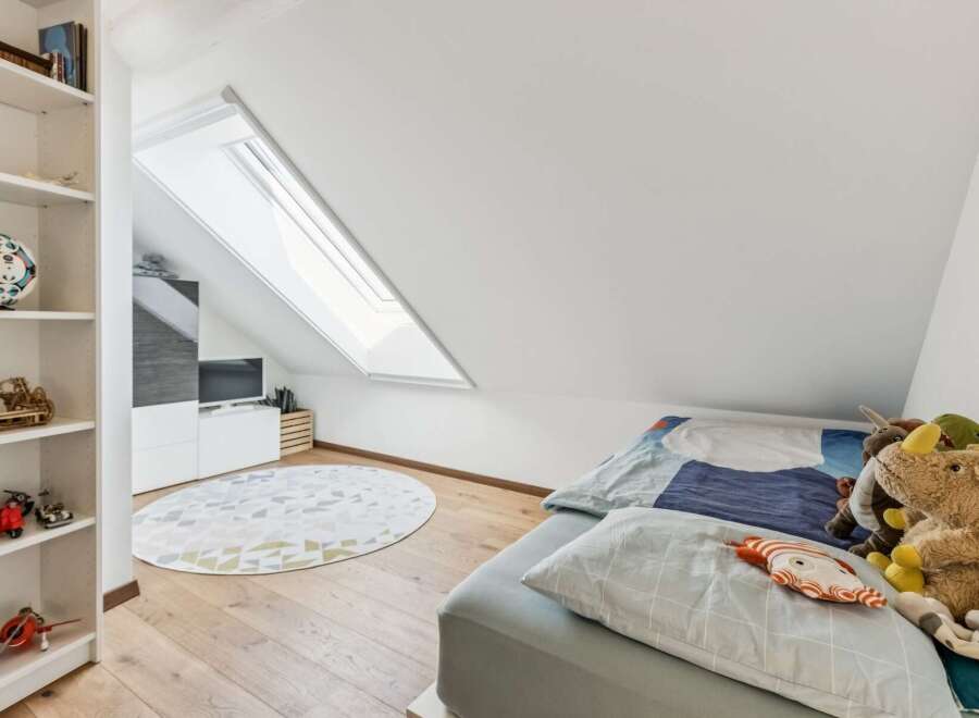 This charming attic bedroom features a cozy bed adorned with playful stuffed animals and a unique patterned duvet.