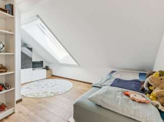 This charming attic bedroom features a cozy bed adorned with playful stuffed animals and a unique patterned duvet.