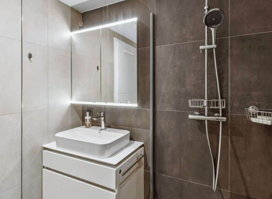 Experience modern comfort in this stylish bathroom featuring a sleek vessel sink atop a white vanity and a well-lit mirror.