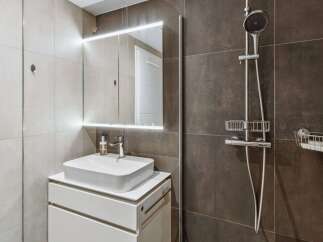 Experience modern comfort in this stylish bathroom featuring a sleek vessel sink atop a white vanity and a well-lit mirror.