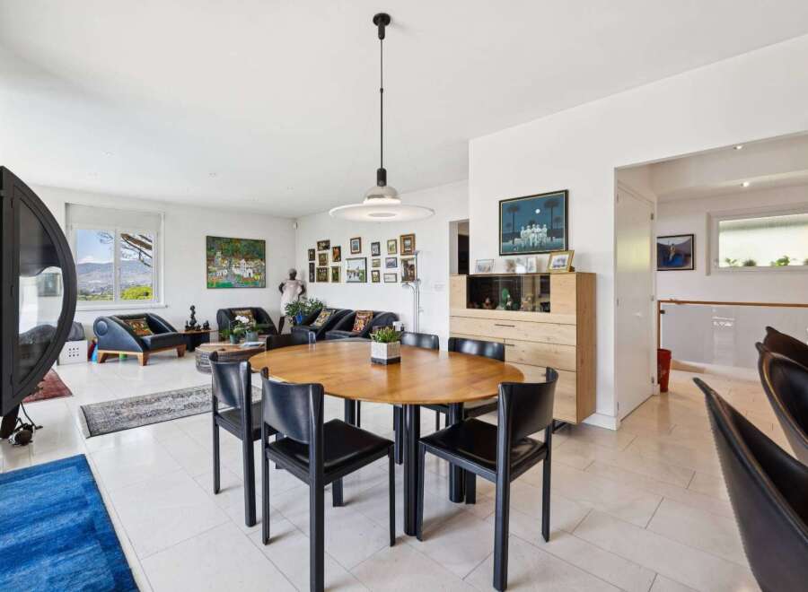 Experience modern living in this spacious open-plan home, featuring a stylish dining area with a round wooden table and black chairs, perfect for family gatherings.
