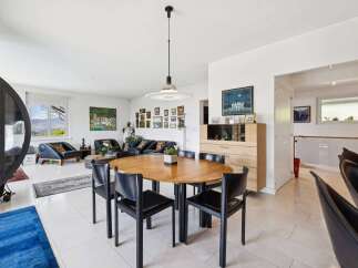 Experience modern living in this spacious open-plan home, featuring a stylish dining area with a round wooden table and black chairs, perfect for family gatherings.