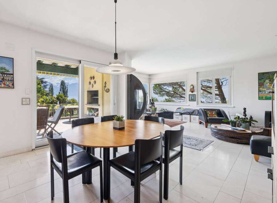 Experience seamless indoor-outdoor living in this spacious dining and living area, featuring a large round wooden dining table with black chairs and direct access to a scenic balcony.