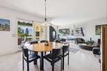 Experience seamless indoor-outdoor living in this spacious dining and living area, featuring a large round wooden dining table with black chairs and direct access to a scenic balcony.