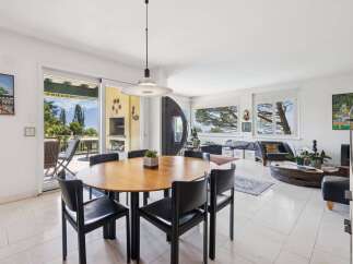 Experience seamless indoor-outdoor living in this spacious dining and living area, featuring a large round wooden dining table with black chairs and direct access to a scenic balcony.