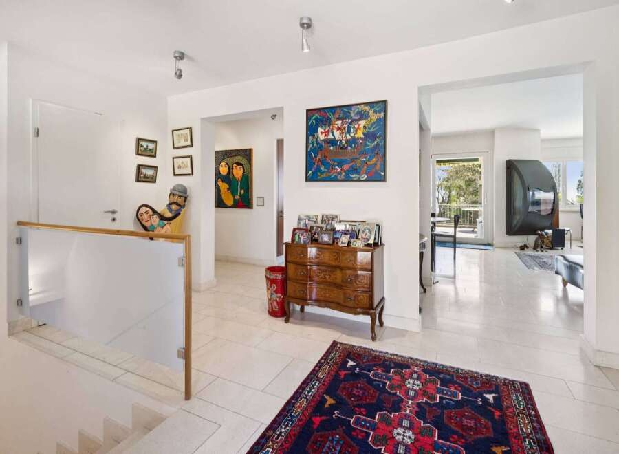 This spacious hallway features a modern glass and wood railing leading down a staircase, complemented by a collection of unique artwork and family photos displayed on the walls.