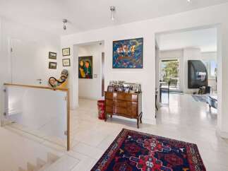 This spacious hallway features a modern glass and wood railing leading down a staircase, complemented by a collection of unique artwork and family photos displayed on the walls.