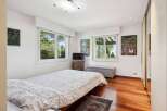 This charming bedroom features a comfortable bed with a patterned duvet, complemented by large windows offering picturesque views of lush greenery.