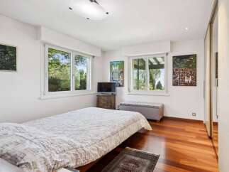 This charming bedroom features a comfortable bed with a patterned duvet, complemented by large windows offering picturesque views of lush greenery.