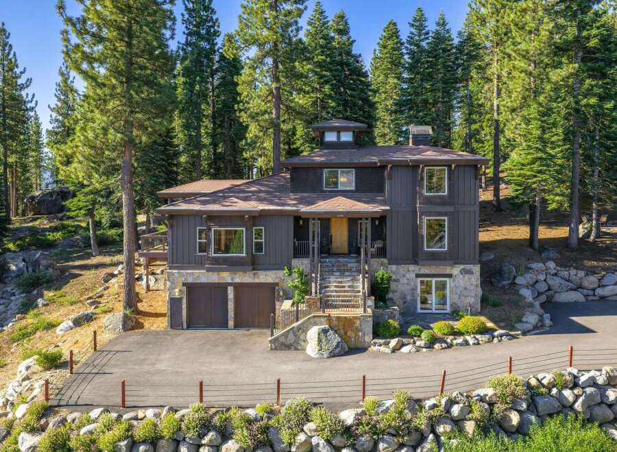 Nestled amidst towering pine trees, this stunning mountain home offers a serene retreat with its natural stone accents and dark wood siding.
