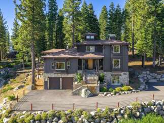 Nestled amidst towering pine trees, this stunning mountain home offers a serene retreat with its natural stone accents and dark wood siding.