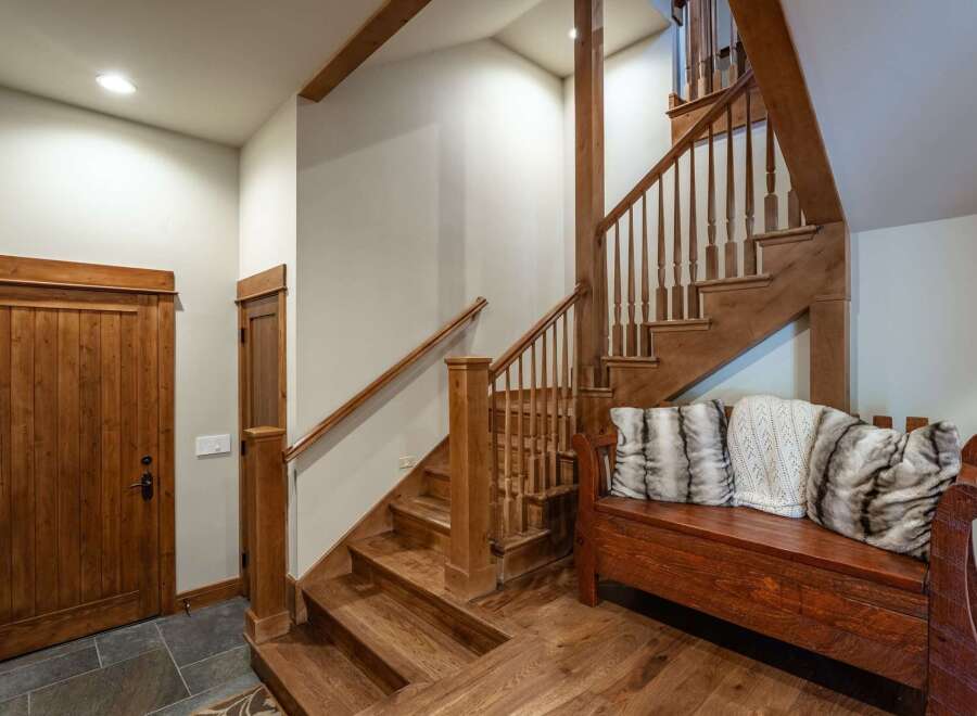 This charming entryway features a rustic wooden staircase with a matching bench adorned with plush pillows, creating a warm and inviting atmosphere.