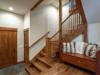 This charming entryway features a rustic wooden staircase with a matching bench adorned with plush pillows, creating a warm and inviting atmosphere.