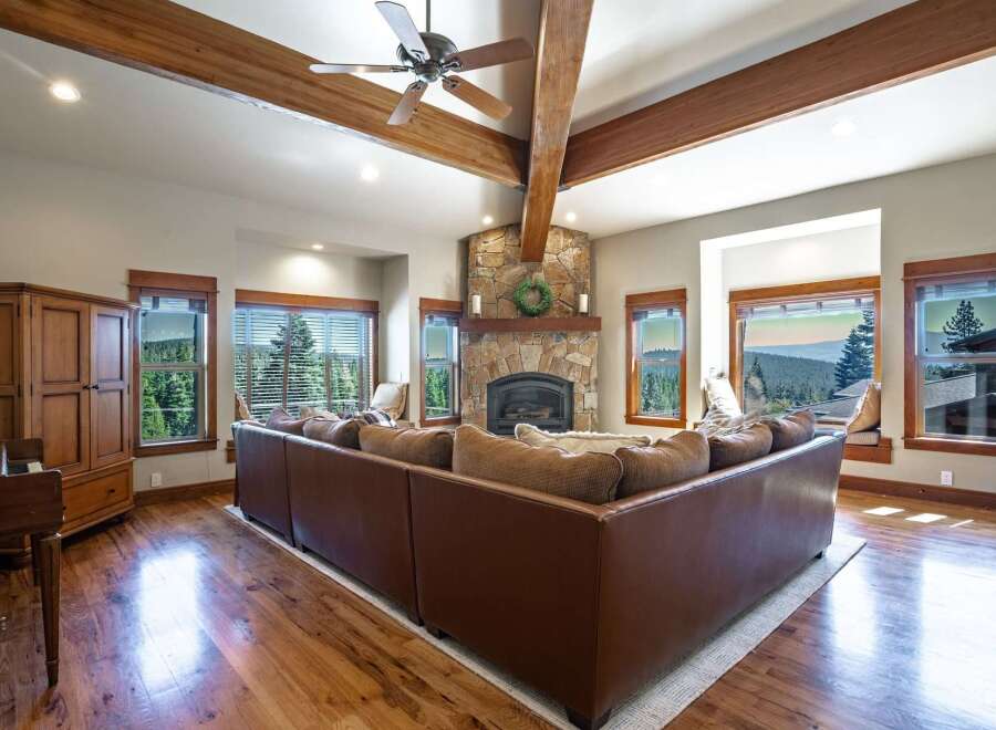 Experience breathtaking mountain views from this stunning living room, featuring a grand stone fireplace and exposed wooden beams.