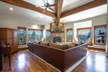 Experience breathtaking mountain views from this stunning living room, featuring a grand stone fireplace and exposed wooden beams.