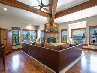 Experience breathtaking mountain views from this stunning living room, featuring a grand stone fireplace and exposed wooden beams.