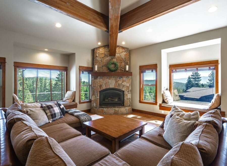 Experience breathtaking mountain views from this stunning living room, featuring a grand stone fireplace and expansive windows.