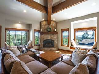 Experience breathtaking mountain views from this stunning living room, featuring a grand stone fireplace and expansive windows.