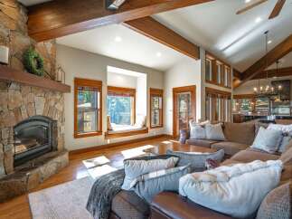 Experience rustic charm in this spacious living room, featuring a grand stone fireplace and exposed wooden beams that add warmth and character.