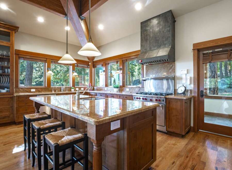 Experience luxury mountain living in this stunning kitchen, featuring a large granite island with bar seating and a professional-grade gas range with a custom hood.